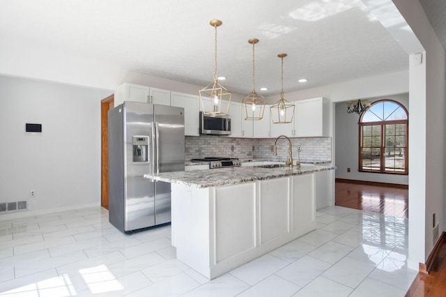 5583 Durrett Rd, Orient, OH 43146 - kitchen with appliances with stainless steel finishes, decorative backsplash, light stone counters, a kitchen island with sink, and hanging light fixtures