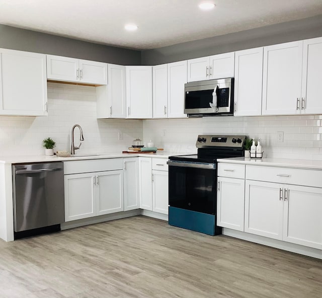 652 E 6th Ave, Lancaster, OH 43130 - kitchen featuring appliances with stainless steel finishes, light countertops, white cabinetry, tasteful backsplash, and light wood-style floors