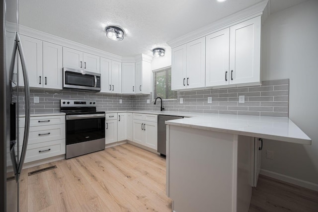 260 Old Coach Pl, Canal Winchester, OH 43110 - kitchen with appliances with stainless steel finishes, a peninsula, light wood-style floors, white cabinetry, and a textured ceiling