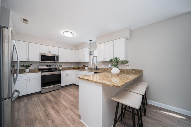 29 Victorian Gate Way, Columbus, OH 43215 - kitchen with stainless steel appliances, a peninsula, wood finished floors, a breakfast bar area, and light stone counters