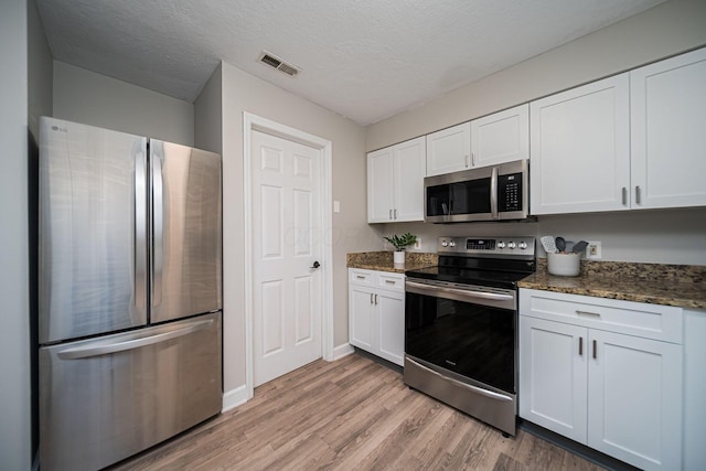 29 Victorian Gate Way, Columbus, OH 43215 - kitchen with appliances with stainless steel finishes, light wood-style flooring, white cabinetry, dark stone counters, and a textured ceiling
