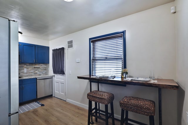 69 Morse Rd, Columbus, OH 43214 - kitchen featuring appliances with stainless steel finishes, blue cabinetry, wood finished floors, decorative backsplash, and a breakfast bar area