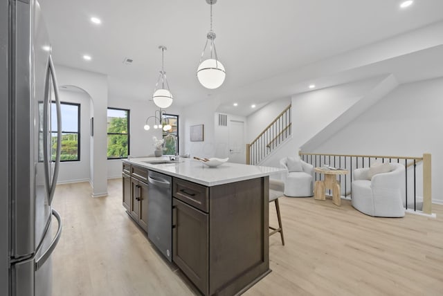 583 E Walnut St, Columbus, OH 43215 - kitchen with stainless steel appliances, dark brown cabinets, open floor plan, light wood finished floors, and a center island with sink