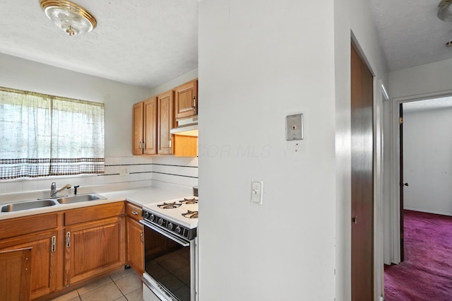 617 Athens St, Columbus, OH 43204 - kitchen with white gas stove, under cabinet range hood, light countertops, brown cabinetry, and light tile patterned flooring