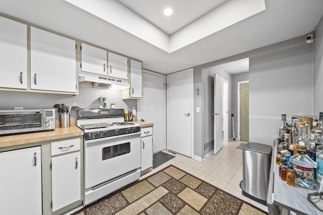 1290 Paddington Ct, Columbus, OH 43230 - kitchen with white gas range, under cabinet range hood, white cabinets, light tile patterned floors, and a tray ceiling