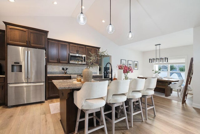 4881 Hoover Rd, Grove City, OH 43123 - kitchen featuring stainless steel appliances, a kitchen bar, light wood finished floors, dark brown cabinetry, and high vaulted ceiling