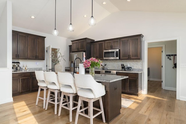 4881 Hoover Rd, Grove City, OH 43123 - kitchen with appliances with stainless steel finishes, lofted ceiling, dark brown cabinetry, a kitchen island with sink, and a kitchen breakfast bar