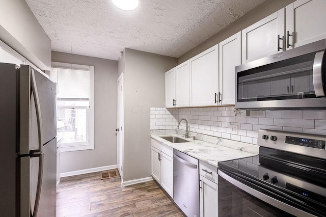211 Buckingham St, Newark, OH 43055 - kitchen featuring stainless steel appliances, light wood finished floors, decorative backsplash, white cabinets, and a textured ceiling
