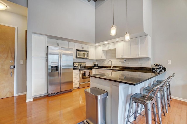 110 N 3rd St Unit 707, Columbus, OH 43215 - kitchen with stainless steel appliances, a peninsula, light wood finished floors, decorative backsplash, and white cabinets