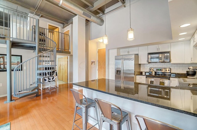 110 N 3rd St Unit 707, Columbus, OH 43215 - kitchen with appliances with stainless steel finishes, a high ceiling, white cabinets, light wood-style flooring, and backsplash