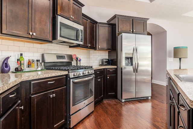 4881 Primrose Ct, Grove City, OH 43123 - kitchen with appliances with stainless steel finishes, dark wood-style floors, backsplash, dark brown cabinets, and arched walkways