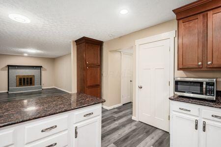 5200 Garmouth Ct, Columbus, OH 43221 - kitchen featuring stainless steel microwave, wood finished floors, dark stone countertops, a fireplace, and a textured ceiling