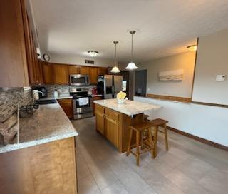 521 Kenton Galion Rd E, Marion, OH 43302 - kitchen featuring stainless steel appliances, brown cabinetry, a center island, and a kitchen breakfast bar