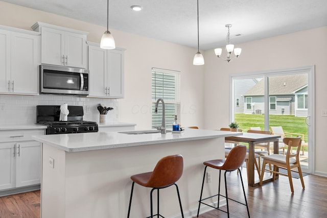 507 Curry Dr, Pataskala, OH 43062 - kitchen featuring stainless steel microwave, range with gas stovetop, decorative backsplash, an island with sink, and light wood-style floors