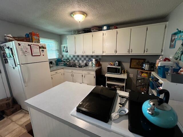 6942 Bartlett Rd, Reynoldsburg, OH 43068 - kitchen featuring freestanding refrigerator, stainless steel microwave, white cabinetry, light countertops, and a textured ceiling