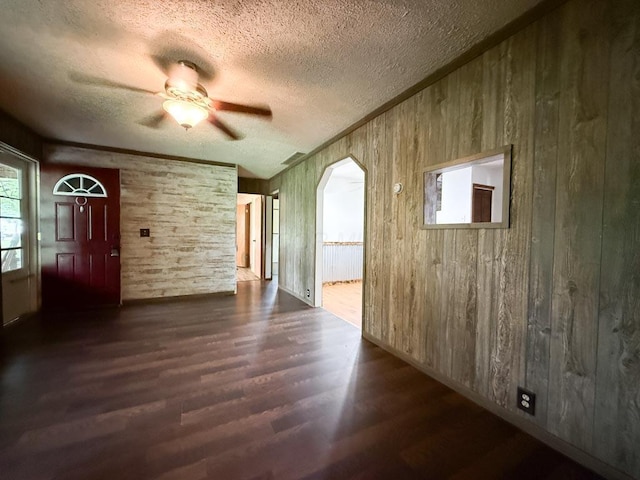 206 William St, Fulton, OH 43321 - unfurnished living room with wood finished floors, a textured ceiling, ceiling fan, wooden walls, and arched walkways