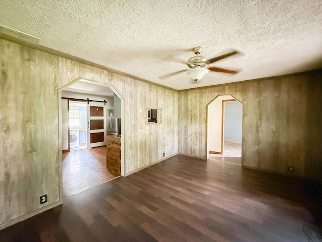 206 William St, Fulton, OH 43321 - empty room featuring dark wood-style flooring, arched walkways, ceiling fan, a barn door, and wooden walls