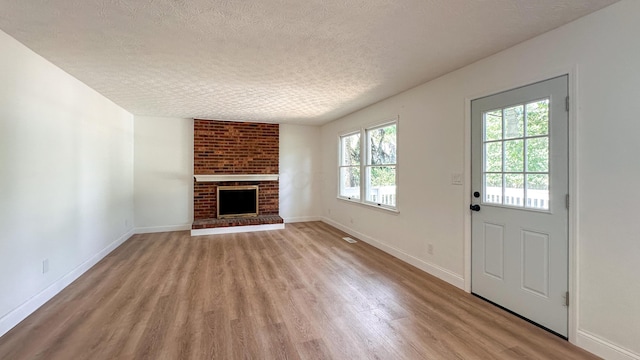5078 Grassland Dr, Dublin, OH 43016 - unfurnished living room with a textured ceiling, light wood-style flooring, and a brick fireplace
