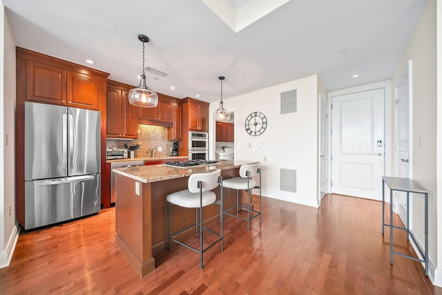 1475 W 3rd Ave Unit 401, Columbus, OH 43212 - kitchen featuring appliances with stainless steel finishes, light wood-style flooring, a kitchen bar, backsplash, and light stone countertops