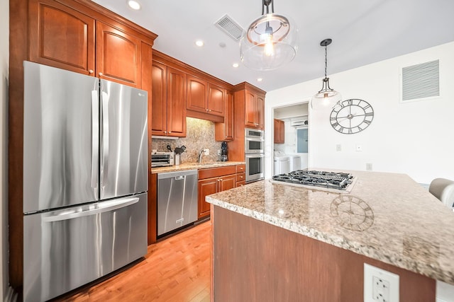 1475 W 3rd Ave Unit 401, Columbus, OH 43212 - kitchen with stainless steel appliances, independent washer and dryer, light wood-style flooring, backsplash, and pendant lighting