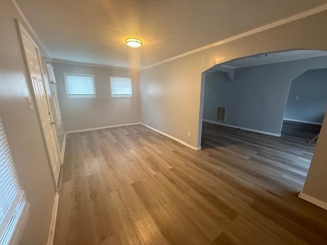 empty room featuring arched walkways, wood finished floors, and crown molding
