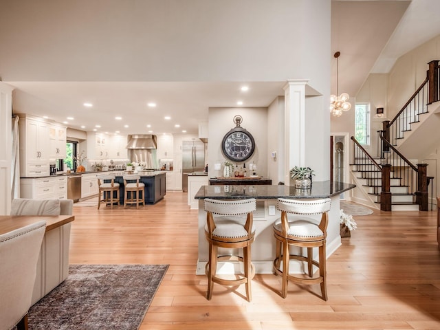 5767 Loch Maree Ct, Dublin, OH 43017 - kitchen featuring a breakfast bar area, light wood-style floors, a spacious island, wall chimney range hood, and white cabinets