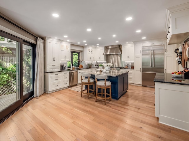 5767 Loch Maree Ct, Dublin, OH 43017 - kitchen featuring stainless steel appliances, white cabinets, backsplash, a kitchen island, and wall chimney exhaust hood