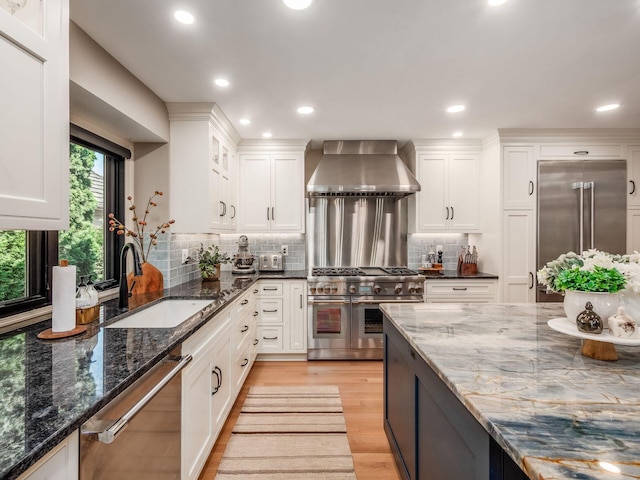 5767 Loch Maree Ct, Dublin, OH 43017 - kitchen featuring high end appliances, wall chimney range hood, white cabinetry, light wood finished floors, and dark stone countertops
