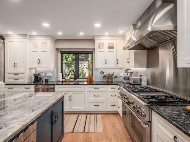 5767 Loch Maree Ct, Dublin, OH 43017 - kitchen featuring appliances with stainless steel finishes, wall chimney range hood, light wood-style flooring, white cabinetry, and backsplash