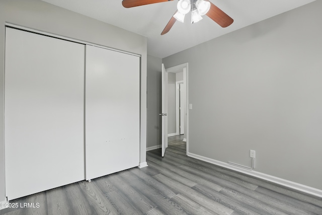 unfurnished bedroom with wood finished floors, a closet, baseboards, and a ceiling fan