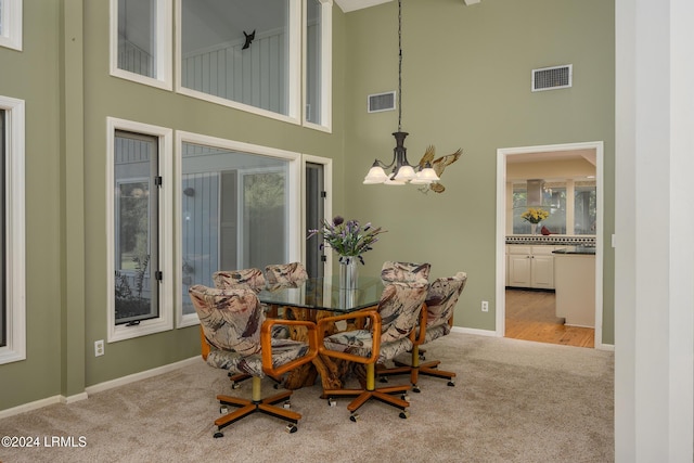 dining room with a towering ceiling, light colored carpet, and a notable chandelier