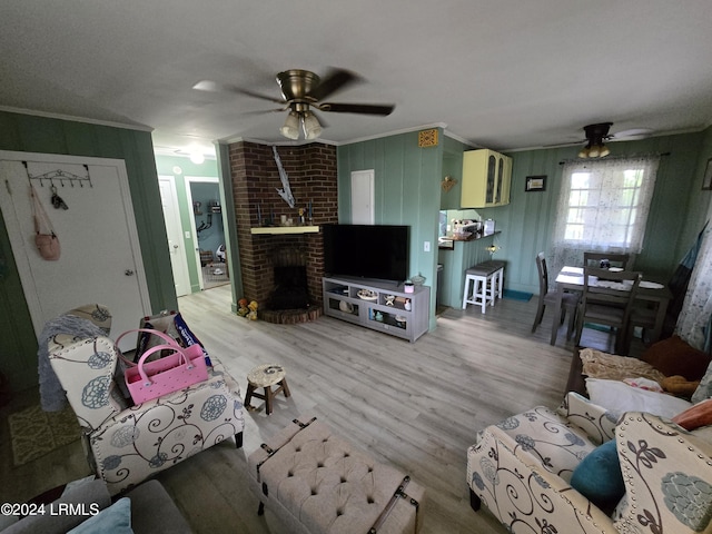 living room with wood-type flooring, a brick fireplace, ornamental molding, wooden walls, and ceiling fan