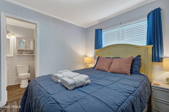 bedroom with wood finished floors, crown molding, and ensuite bath
