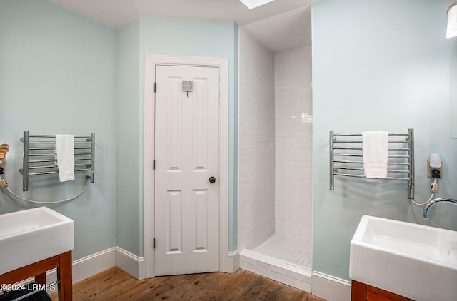 bathroom with a tile shower, sink, radiator heating unit, and wood-type flooring