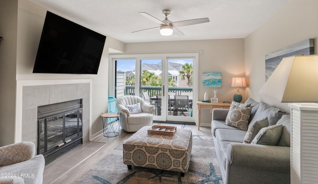 living room featuring a tiled fireplace, a textured ceiling, light hardwood / wood-style floors, and ceiling fan