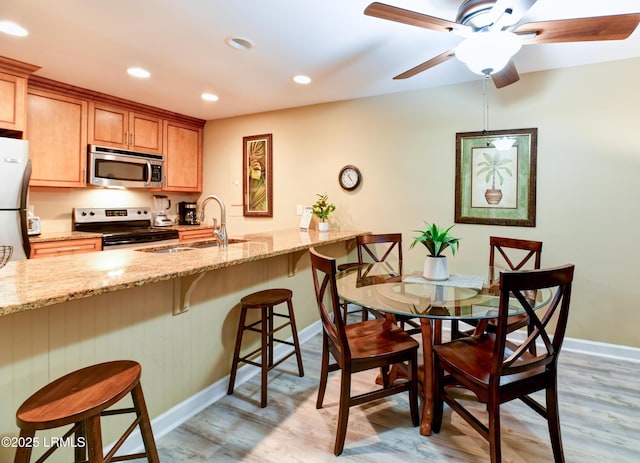 kitchen with a kitchen bar, sink, light stone counters, light wood-type flooring, and appliances with stainless steel finishes