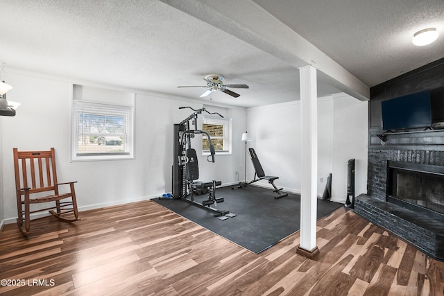 workout room featuring wood-type flooring, a brick fireplace, ceiling fan, and a textured ceiling