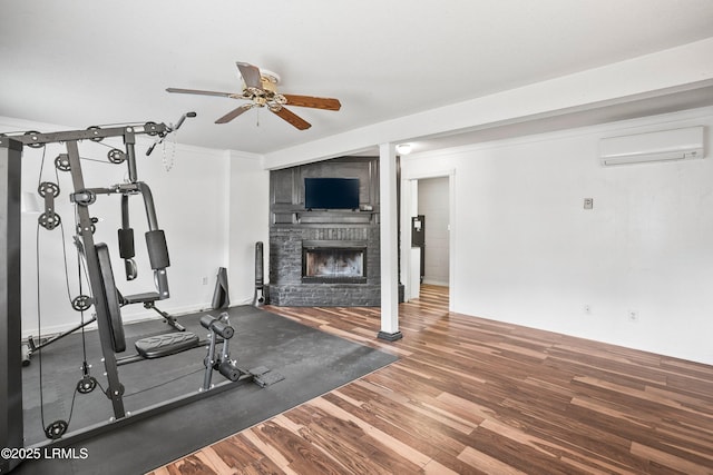 exercise area with ceiling fan, a wall mounted air conditioner, a stone fireplace, and hardwood / wood-style floors