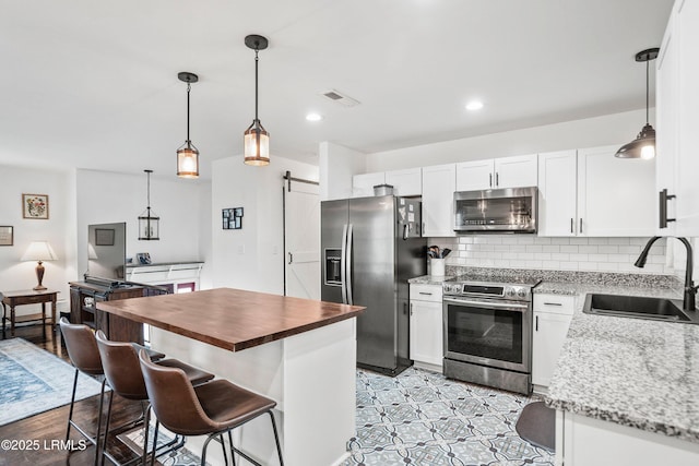 kitchen with sink, appliances with stainless steel finishes, pendant lighting, a barn door, and white cabinets