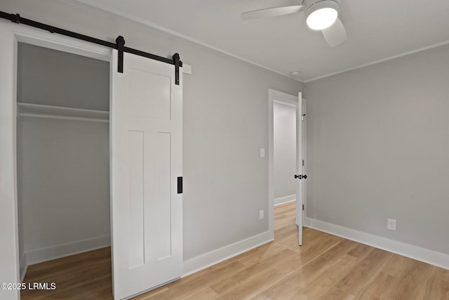 unfurnished bedroom with baseboards, ornamental molding, light wood-type flooring, and a barn door