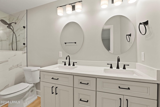 bathroom featuring double vanity, toilet, a marble finish shower, and a sink