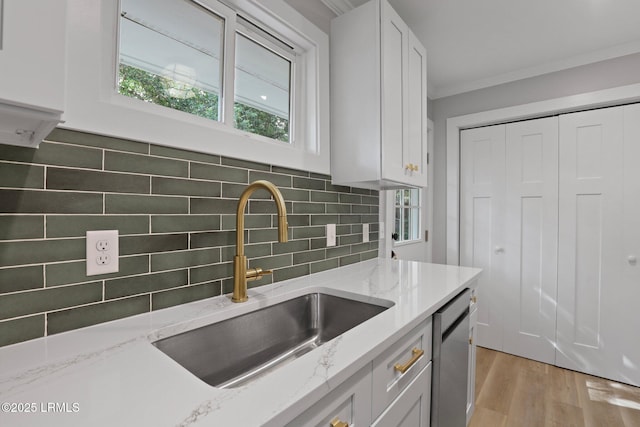 kitchen featuring crown molding, a sink, backsplash, white cabinetry, and stainless steel dishwasher