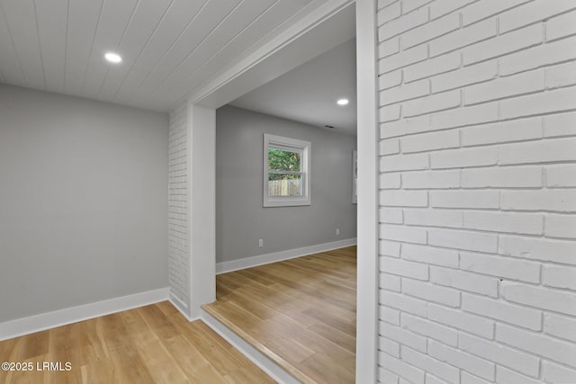 hallway featuring brick wall, baseboards, recessed lighting, and light wood-style flooring
