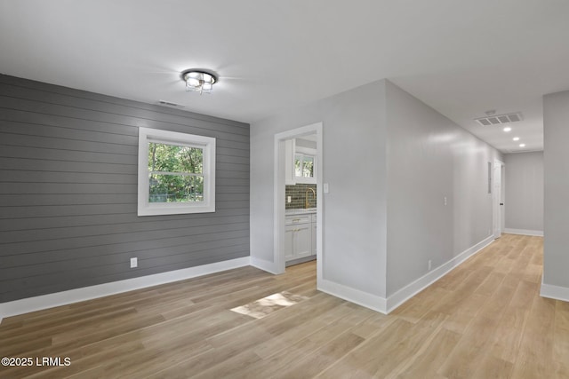 unfurnished room with baseboards, a sink, light wood finished floors, and visible vents