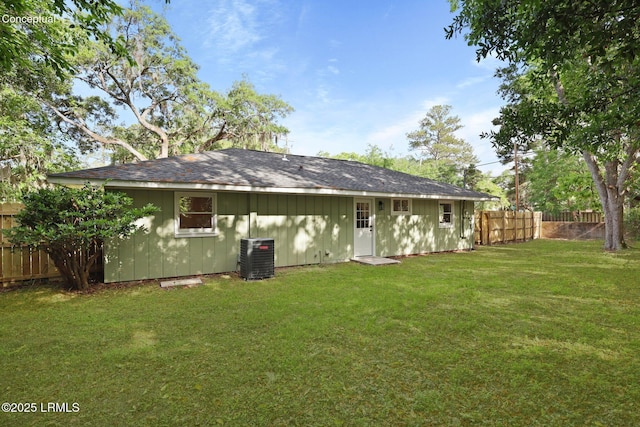 rear view of house with fence, a shingled roof, board and batten siding, central AC unit, and a yard