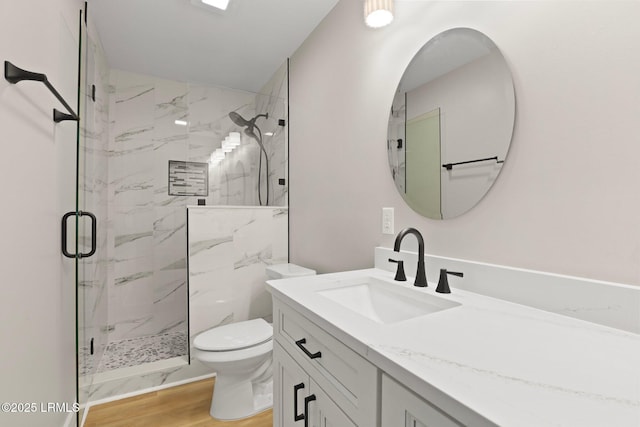 bathroom with a marble finish shower, vanity, toilet, and wood finished floors
