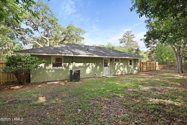 rear view of property featuring roof with shingles, central AC, board and batten siding, a fenced backyard, and a lawn