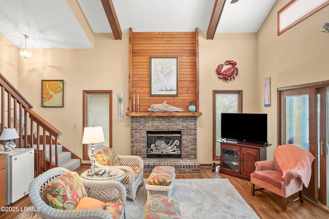 living room featuring stairs, a towering ceiling, wood finished floors, a fireplace, and beamed ceiling