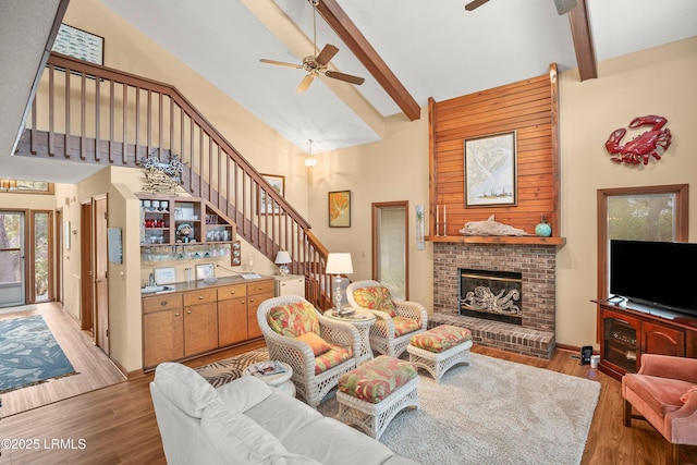 living room featuring a ceiling fan, beam ceiling, wood finished floors, stairway, and high vaulted ceiling