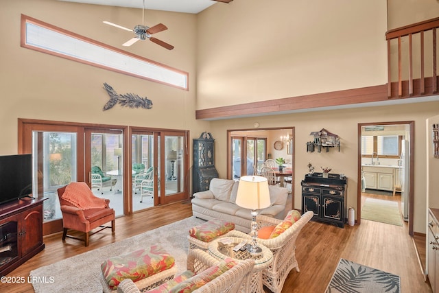 living area with a high ceiling, a ceiling fan, and light wood-type flooring